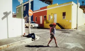 Une jeune fille porte son petit frère dans cette photo de rue colorée. Un homme dort sur le trottoir.