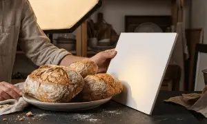 Une photo culinaire met en scène des pains artisanaux sur une assiette, éclairés par une douce lumière. Un réflecteur blanc est tenu pour parfaire la mise en scène.