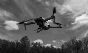 Un drone survole une forêt sous un ciel nuageux.