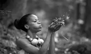 Une femme souffle sur des herbes dans cette technologie image noir et blanc. Elle porte un collier de perles rondes.
