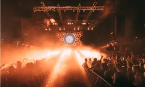 Foule en délire sous les lumières oranges d'une scène, un visuel psychédélique au centre. Photographie événementielle capturant l'énergie d'un concert.