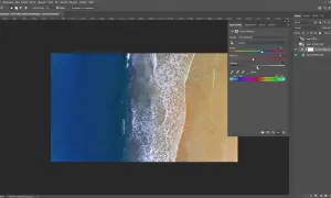 Un homme ajuste les curseurs de teinte, saturation et luminosité dans Photoshop pour changer la couleur d'une photo de plage.
