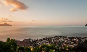 Coucher de soleil sur une plage de galets, avec des îles au loin. Les **filtres photo** accentuent les tons pastel du ciel et la douceur de l'eau.