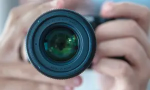 Gros plan sur un objectif d'appareil photo tenu par des mains. La mise au point photographie est parfaite, révélant les reflets verts dans la lentille.