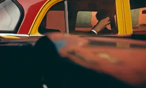 Vue à travers une fenêtre de voiture rouge et jaune, la main d'un homme au volant, typique des saul leiter photos.