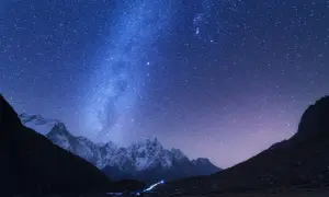 Magnifique photo de nuit. Le ciel étoilé scintille au-dessus de montagnes enneigées et d'un petit village illuminé.