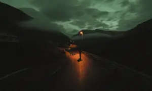Une silhouette solitaire sur une route de montagne, éclairée par un lampadaire. Le ciel est sombre et nuageux, donnant à cette **grain photo en ligne** une atmosphère mystérieuse.