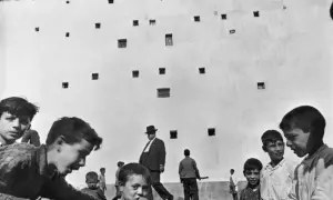 Enfants jouant devant un mur criblé de fenêtres, un homme en chapeau traverse cette photo historique célèbre.