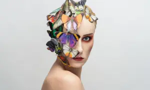 Portrait d'une femme au maquillage audacieux, ornée de papillons colorés sur la tête et le visage, évoquant une **flora borsi** onirique.