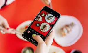 Une main ajuste le paramètre appareil photo Android pour photographier des sushis appétissants sur une table rouge vif.