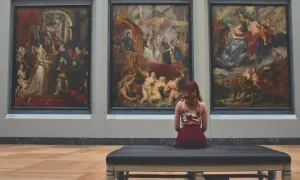 Une femme assise sur un banc, contemplant trois tableaux baroques. L'analyse photo révèle une scène de musée immersive.