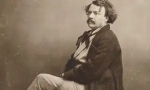 Portrait photographique 19ème siècle d'un homme à la moustache et aux cheveux bouclés, vêtu d'un manteau sombre et d'une chemise à nœud.