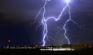 Un spectaculaire **photo orage** illumine le ciel nocturne au-dessus d'un aéroport. Des éclairs zèbrent l'obscurité, illuminant les bâtiments et les lumières de piste.