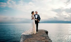 Un couple de jeunes mariés, vêtus de leurs tenues de mariage, pose sur un promontoire rocheux face à la mer. Ces photos de mariage capturent un moment de sérénité.