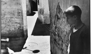 Un jeune garçon se tient dans une ruelle étroite, une ombre projetée sur le sol. Une scène typique des henri cartier bresson photos célèbres.