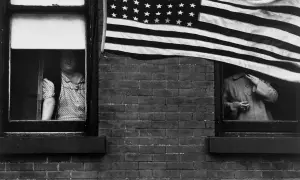 Une photographe femme américaine capture deux femmes regardant par des fenêtres, un drapeau américain flottant au-dessus.