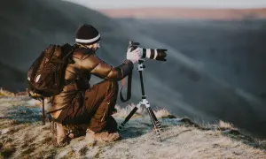 Un homme, peut-être le plus grand photographe du monde, s'accroupit sur une colline gelée, ajustant son appareil photo professionnel sur un trépied pour capturer le paysage.