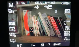 Livres sur une étagère, avec des lignes rouges indiquant le **focus peaking** sur les bords des livres. Réglages de l'appareil photo visibles.