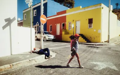 Une jeune fille porte son petit frère dans cette photo de rue colorée. Un homme dort sur le trottoir.