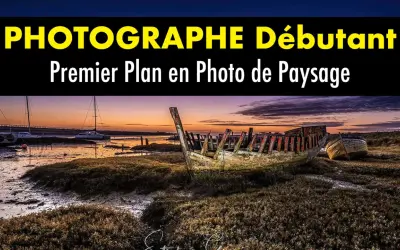 Épave de bateau en premier plan sur une plage au coucher du soleil. Au loin, des voiliers et un pont.
