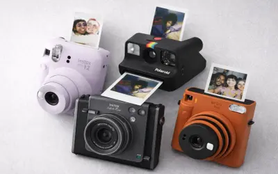 Quatre appareils photo instantanés, dont un Instax Mini 12 lilas, un Polaroid noir et un Instax orange, sortent des photos de souvenirs.