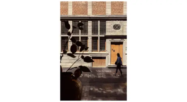 Photographie architecture : une femme passe devant une façade historique aux fenêtres multiples et à la porte en bois.