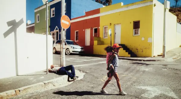 Une jeune fille porte son petit frère dans cette photo de rue colorée. Un homme dort sur le trottoir.