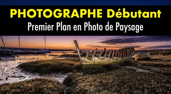 Épave de bateau en premier plan sur une plage au coucher du soleil. Au loin, des voiliers et un pont.
