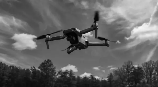 Un drone survole une forêt sous un ciel nuageux.