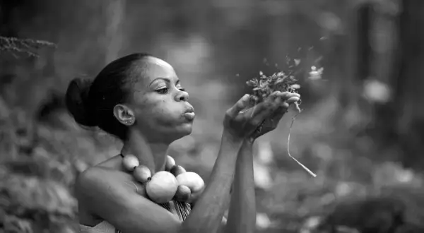Une femme souffle sur des herbes dans cette technologie image noir et blanc. Elle porte un collier de perles rondes.