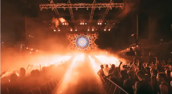 Foule en délire sous les lumières oranges d'une scène, un visuel psychédélique au centre. Photographie événementielle capturant l'énergie d'un concert.