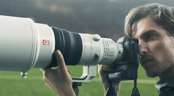 Photographe sportif utilisant un appareil photo Sony a9 II avec un téléobjectif blanc, prêt à capturer l'action sur le terrain.