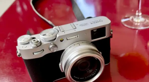 Appareil photo argenté Fujifilm X100VI sur fond rouge vif, prêt pour un test.