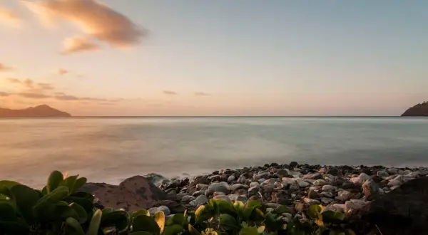 Coucher de soleil sur une plage de galets, avec des îles au loin. Les **filtres photo** accentuent les tons pastel du ciel et la douceur de l'eau.