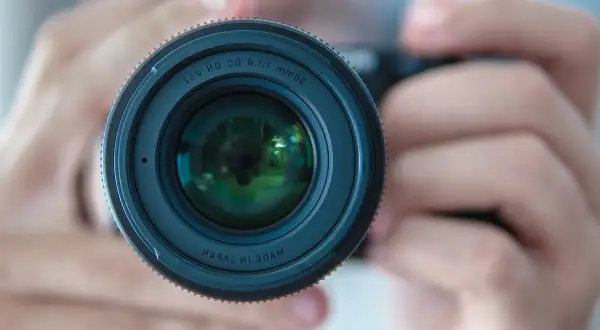 Gros plan sur un objectif d'appareil photo tenu par des mains. La mise au point photographie est parfaite, révélant les reflets verts dans la lentille.