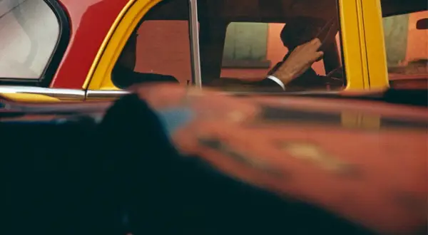 Vue à travers une fenêtre de voiture rouge et jaune, la main d'un homme au volant, typique des saul leiter photos.
