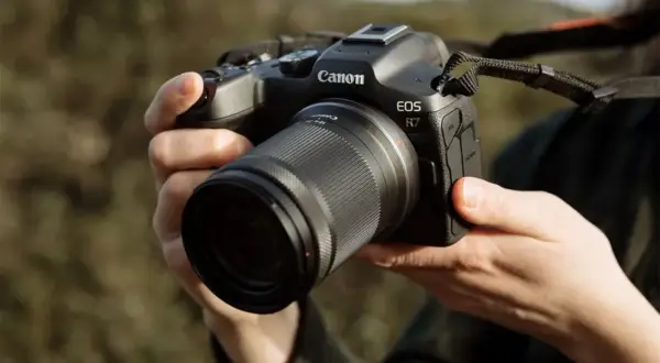 Mains tenant un appareil photo Canon EOS R7 avec un objectif. Prêt à capturer la beauté de la nature.