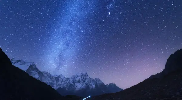 Magnifique photo de nuit. Le ciel étoilé scintille au-dessus de montagnes enneigées et d'un petit village illuminé.