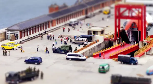 Scène de port avec des véhicules et des personnes, effet tilt shift donnant une impression de maquette.