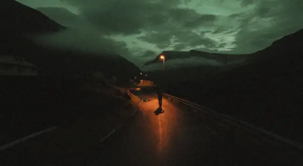Une silhouette solitaire sur une route de montagne, éclairée par un lampadaire. Le ciel est sombre et nuageux, donnant à cette **grain photo en ligne** une atmosphère mystérieuse.