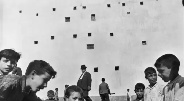 Enfants jouant devant un mur criblé de fenêtres, un homme en chapeau traverse cette photo historique célèbre.