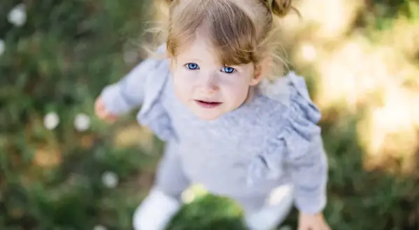 Un bébé aux yeux bleus vifs, coiffé de couettes, regarde vers le ciel. Le flouter arrière plan photo met en valeur son visage innocent.