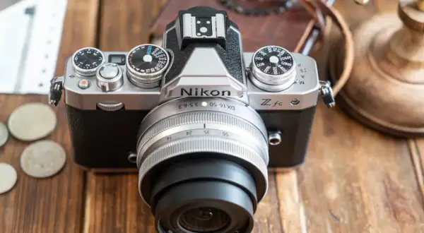Un appareil photo Nikon Zfc argenté et noir, prêt pour un avis. Des pièces et des billets sont à côté.