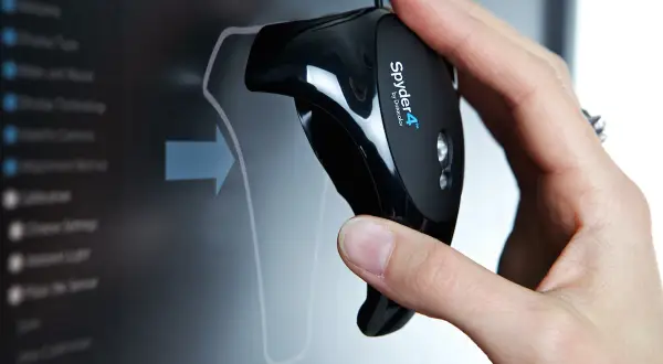 Main d'une personne tenant un appareil Spyder4 pour calibrer ecran pc. L'écran affiche un menu de calibration.