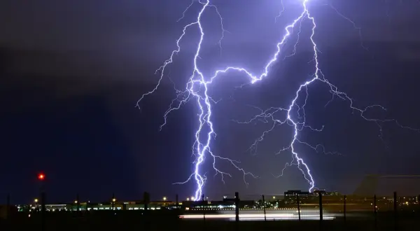 Un spectaculaire **photo orage** illumine le ciel nocturne au-dessus d'un aéroport. Des éclairs zèbrent l'obscurité, illuminant les bâtiments et les lumières de piste.