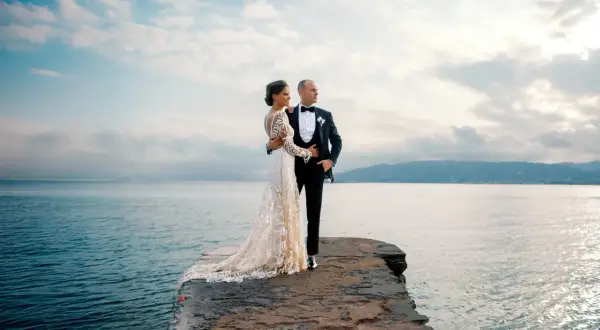 Un couple de jeunes mariés, vêtus de leurs tenues de mariage, pose sur un promontoire rocheux face à la mer. Ces photos de mariage capturent un moment de sérénité.