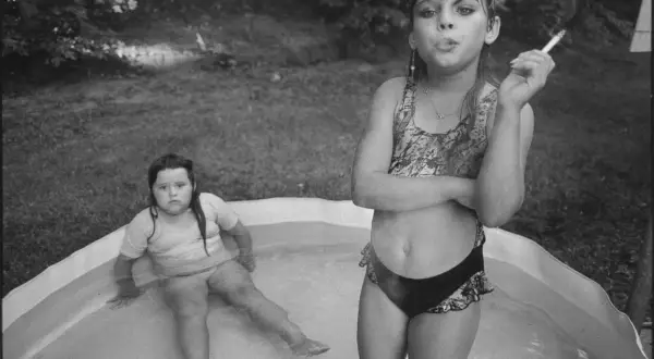 Deux jeunes filles dans une piscine gonflable, l'une fumant une cigarette, dans le style de Mary Ellen Mark.