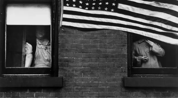 Une photographe femme américaine capture deux femmes regardant par des fenêtres, un drapeau américain flottant au-dessus.