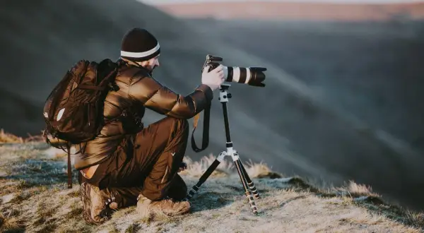 Un homme, peut-être le plus grand photographe du monde, s'accroupit sur une colline gelée, ajustant son appareil photo professionnel sur un trépied pour capturer le paysage.