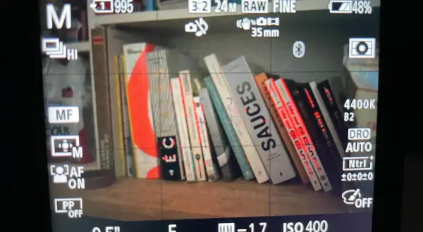 Livres sur une étagère, avec des lignes rouges indiquant le **focus peaking** sur les bords des livres. Réglages de l'appareil photo visibles.